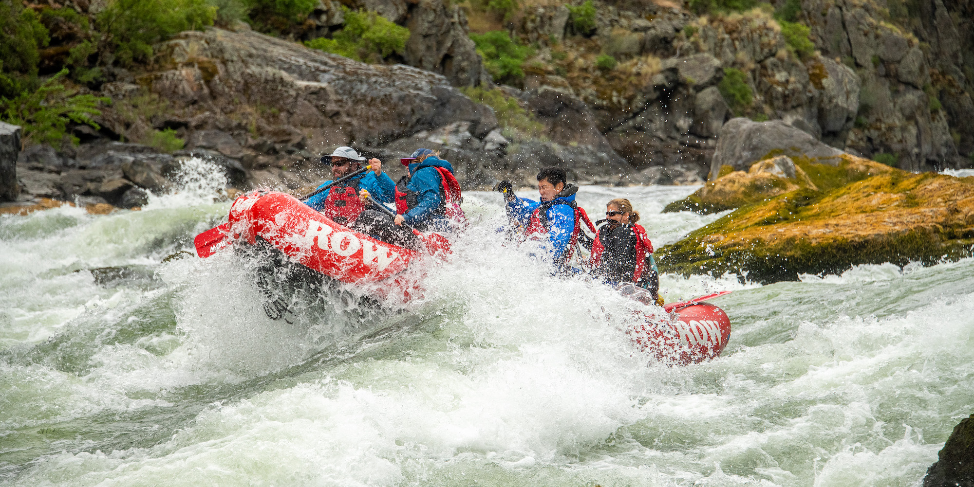 A group of people on a red raft paddling through a class IV rapid on the Snake River through Hells Canyon