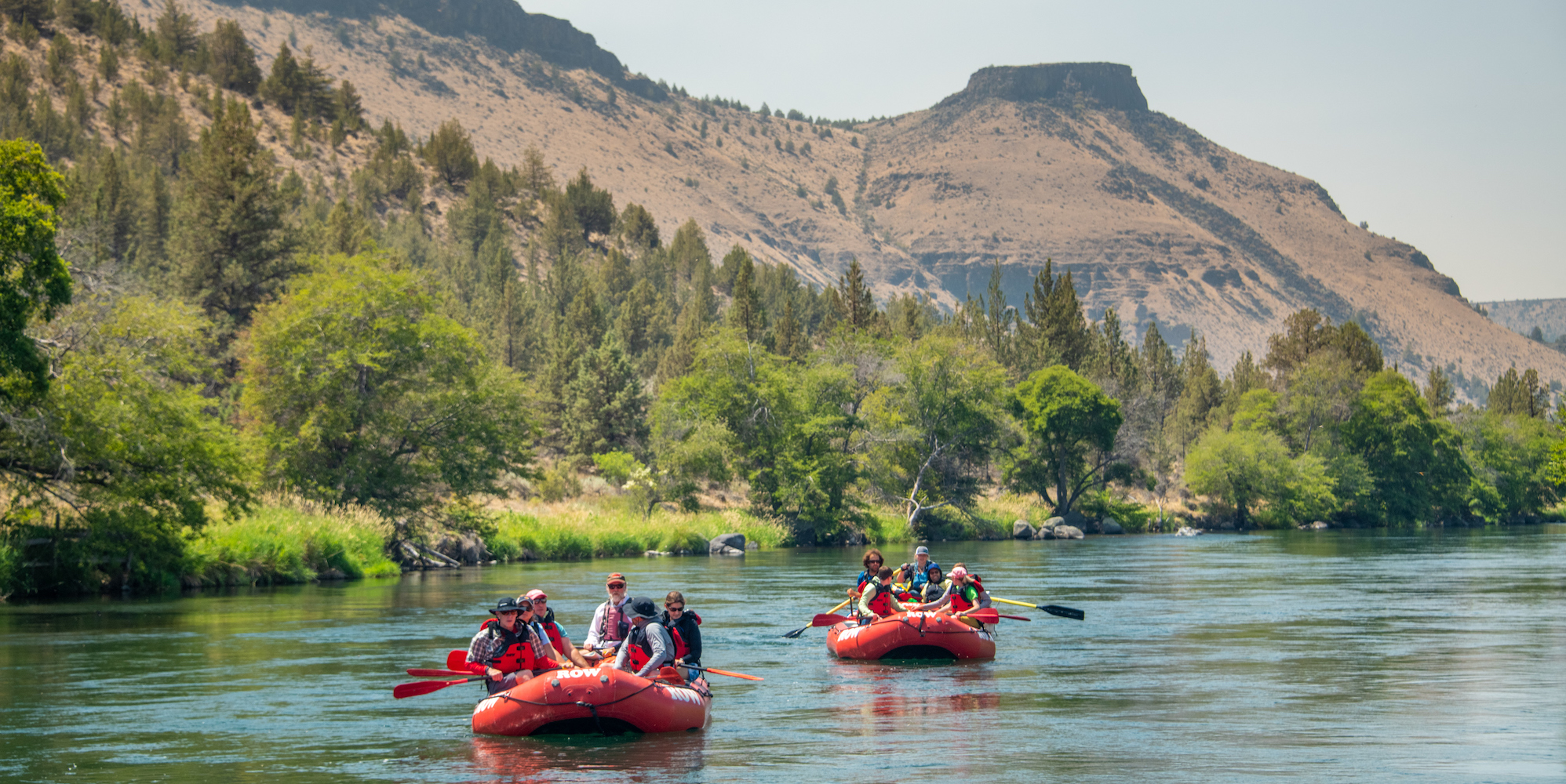 Two red rafts full of passengers paddling down the Deschutes River on a sunny summer day