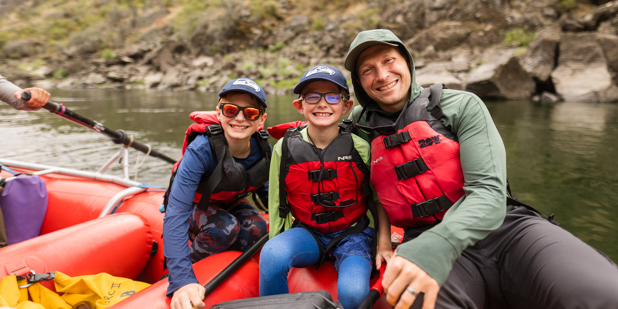 A dad and his two sons sitting on a red raft on the Lower Salmon River in Idaho