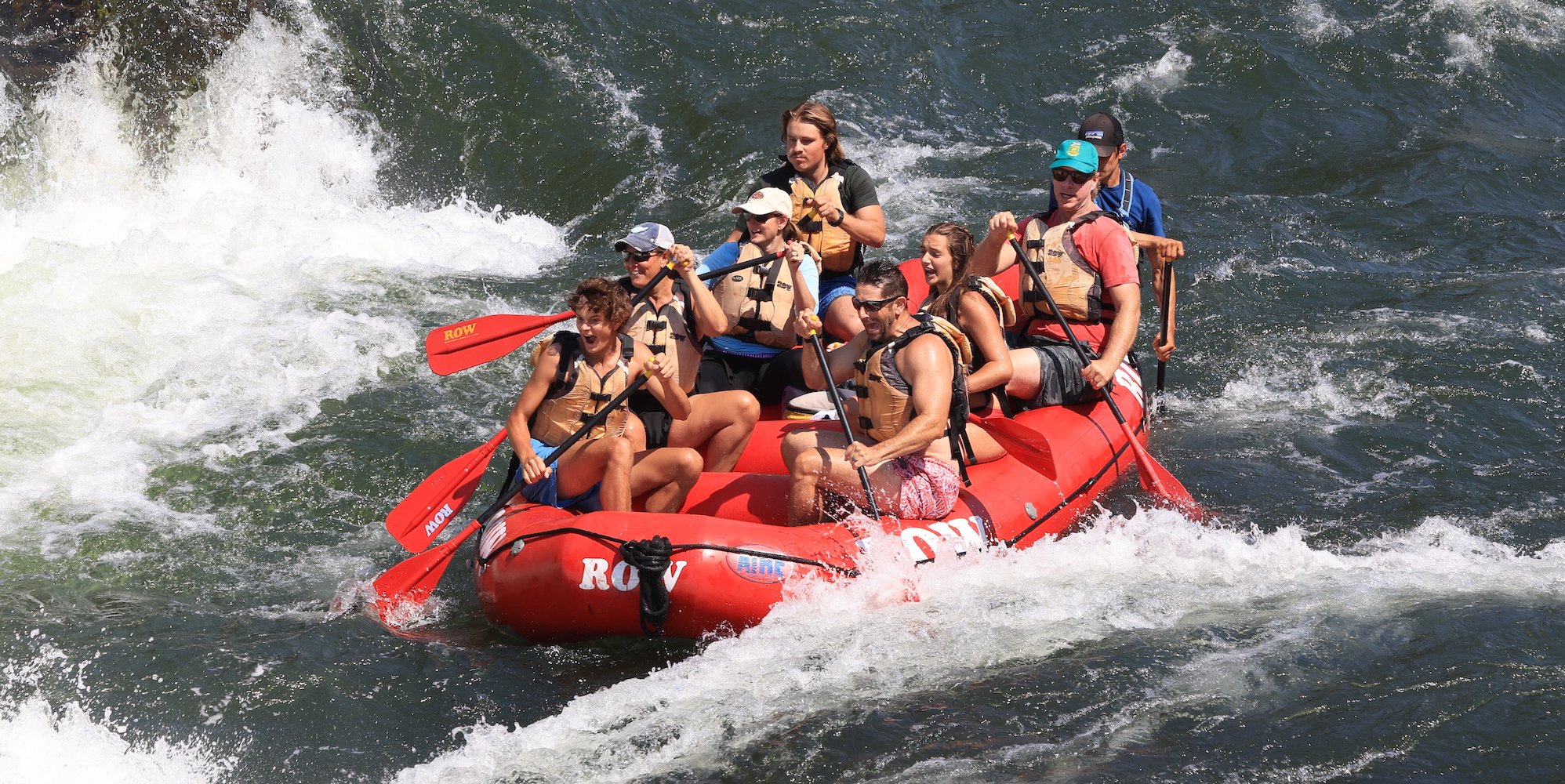 Group of whitewater rafters in a red raft paddling through a rapid on the Clark Fork river in Missoula, Montana