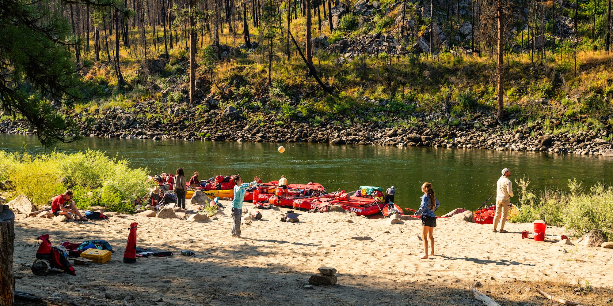 Rafters prepare gear and play on a sandy beach campsite beside the Main Salmon River during a guided rafting trip