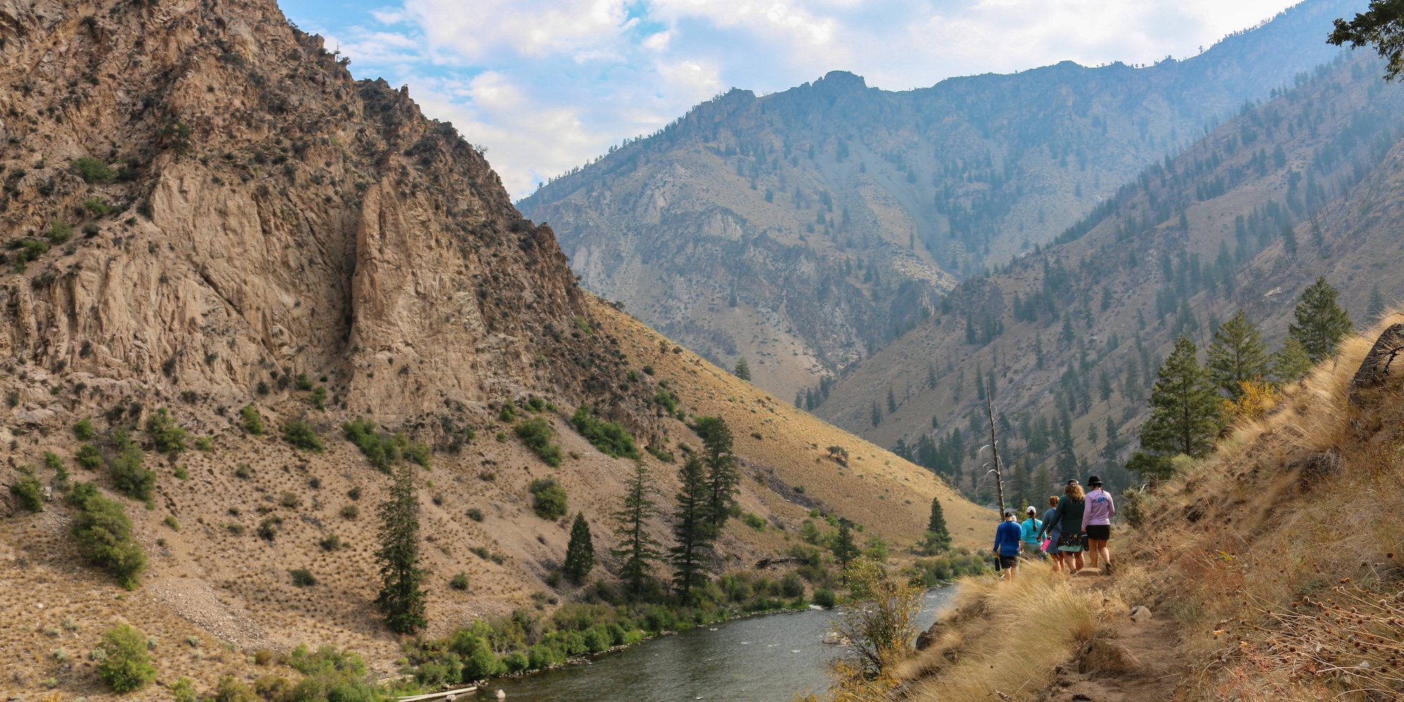 Rafters hiking a canyon trail above the Middle Fork of the Salmon River, overlooking steep walls and winding water through Idaho wilderness.