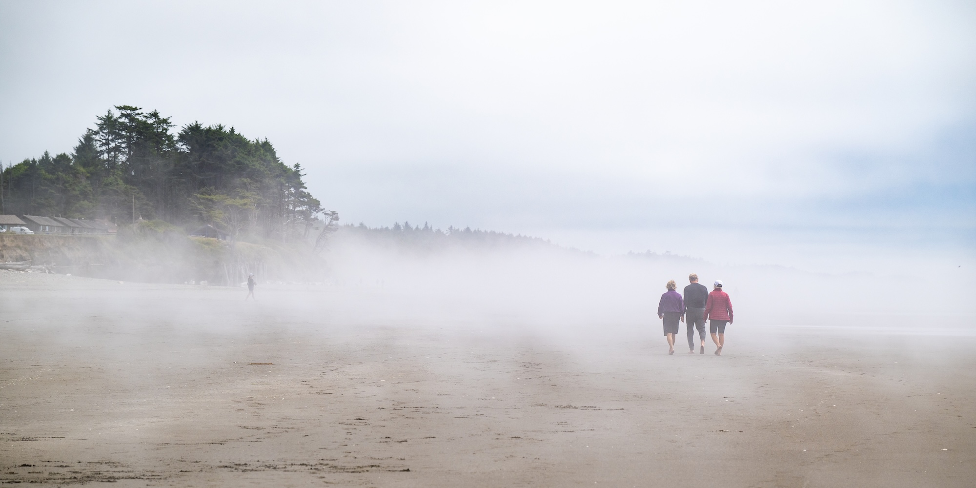 Visitors walking through coastal fog on the Olympic Peninsula, showcasing the unpredictable weather along Washington’s beaches.